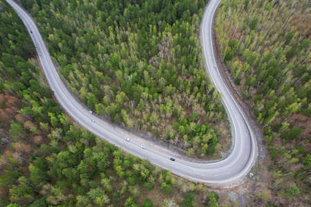 Aerial view of the serpentine highway. Cars drive on a road through the spring forest.