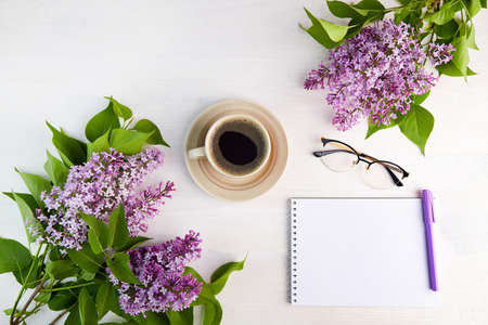 Lilac branches, cup of coffee, notebook with pen on a white wooden background. Spring background.の写真素材