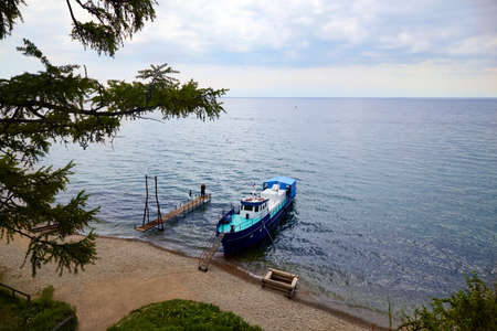 Lake Baikal on a cloudy summer day. The ship is at the shore of the lake, a romantic couple is hugging on the pier.の写真素材