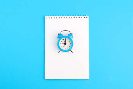 Classic alarm clock and empty notepad on blue background. Top view, copy space.の写真素材