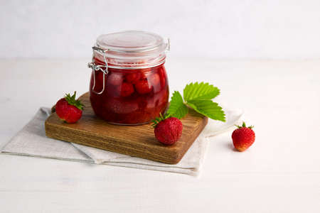 Strawberry jam in a glass jar with fresh berries on white wooden background. Homemade strawberry...