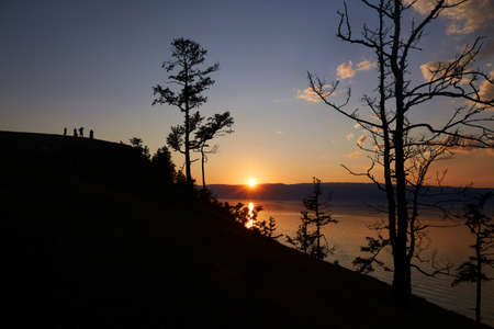 People are standing on a rock and admiring the sunset. Silhouettes of people and trees at an orange...
