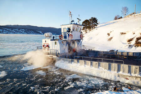 Ferry for the transportation of passengers, tourists and cargo near the shore. Melting ice and open water in the lake.の写真素材
