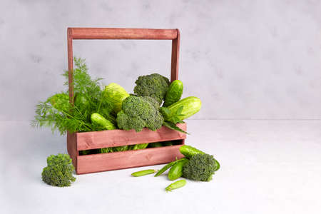 Green vegetables in a wooden box on a gray background. Zucchini, cucumber, pepper, broccoli, dill, green peas. No plastic. Zero wasteの写真素材