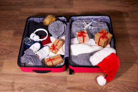 Packing luggage, preparing things for a trip for Christmas. A suitcase with warm clothes, passport,...