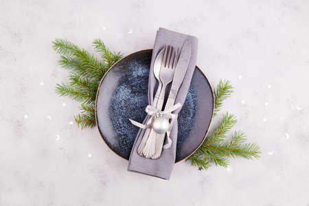 Christmas table setting. Vintage plate, silverware, fir branches, festive decor on a light gray...