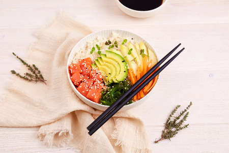 Poke bowl with salmon, rice, avocado, mango, seaweed, carrot, sesame seeds and soy sauce. Hawaiian diet food with fish.の写真素材