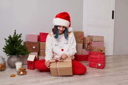 A happy girl in pajamas and a red Santa hat opens Christmas gifts.の写真素材