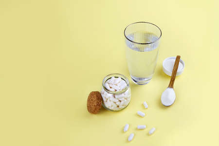 Collagen protein powder and pills in jars, a glass of water on a light yellow background. Dietary supplement for skin and joints. High quality photoの写真素材