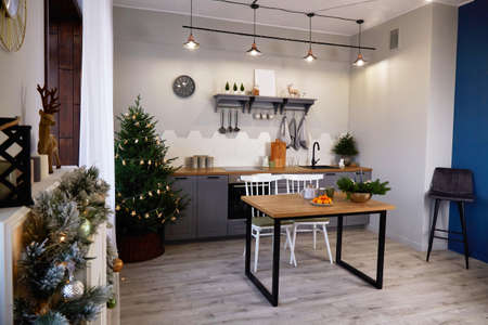 Christmas home interior. The living room and kitchen are decorated for a holiday. Christmas tree with a garland, decorated fireplace. Modern kitchen.の写真素材