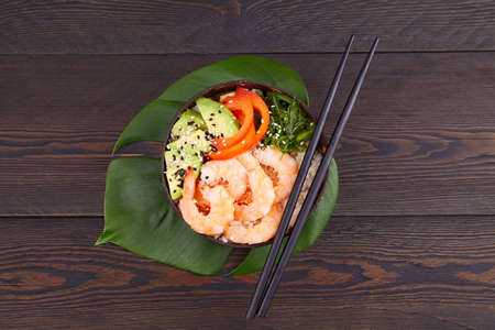 Poke a bowl with shrimp, avocado, rice, pepper, chuka seaweed on a dark wooden background. Top view.の写真素材