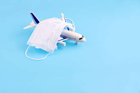 Airplane toy and face mask on blue background. Traveling during virus disease prevention concept. Copy space.の写真素材
