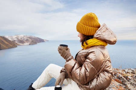 A young girl is a traveler at a rest stop. Admiring the beautiful winter landscape, drinking hot...