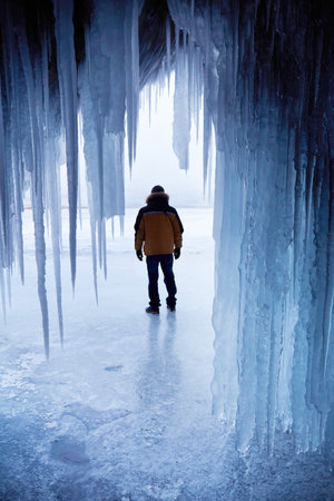 View from an ice cave with icicles on the frozen Lake Baikal. A man travels in winter.