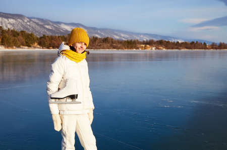 Portrait of a smiling female athlete with figure skates on the background of frozen Lake Baikal. Active recreation, unity with nature, outdoor sports, natural background.の写真素材