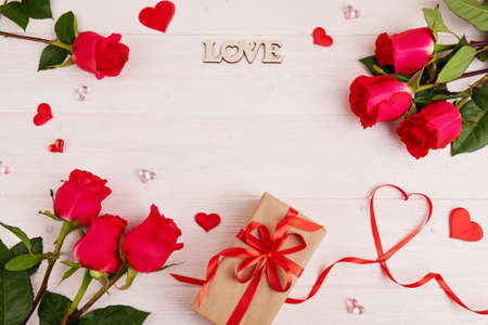 Red roses, a gift box made of craft paper with a red ribbon, the inscription love on a white wooden background. Valentine's Day, Mother's Day, Birthday. Top view, copy space.の写真素材