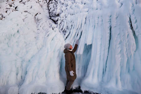 A woman looks at the huge icicles on the rocks of the island of Oltrek. Winter trip on Lake Baikal.