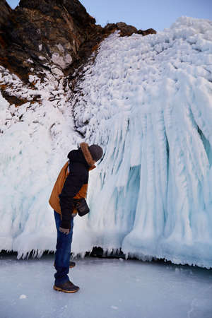 A man is traveling on the frozen Lake Baikal. A tourist looks at the statues or icicles on the rocks of the Island of Olkhon, Ogoy, Oltrek in winter. vertical orientation.の写真素材