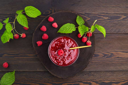 Raspberry jam in a glass bowl and fresh berries on a dark wooden background.