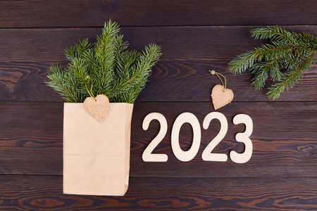 Happy New Year 2023 Greeting Card. Winter bouquet of fir branches in a craft bag. Wooden numbers 2023. Eco-friendly packaging, zero waste.の写真素材