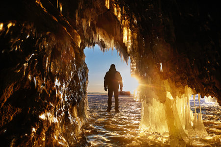 A man stands by a rock with huge icicles. Winter trip on Lake Baikal.