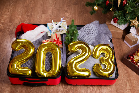 Happy New Year 2023. Golden balloons with numbers. An open suitcase