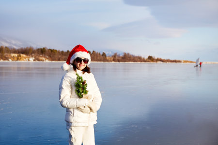 A girl in a Santa Claus hat and sunglasses holds a small Christmas treeの写真素材