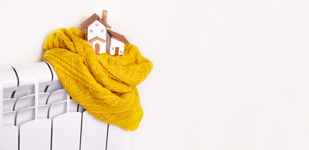 Toy wooden houses, knitted scarf on the central heating battery in the apartment. The concept of a heating system, cold winter season, energy saving, economical heating of the house. Bannerの写真素材