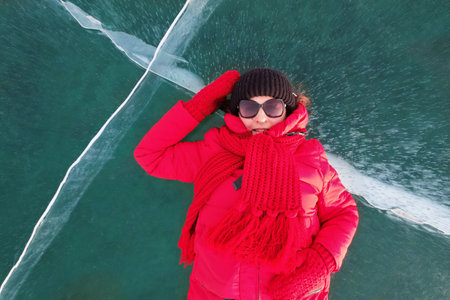 A female tourist in a red down jacket on the background of transparent iceの写真素材