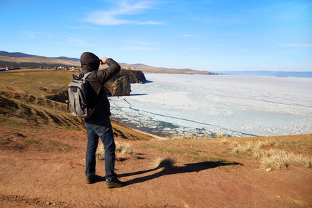 A male traveler enjoys a beautiful view of Lake Baikal during the melting of ice. spring landscape....