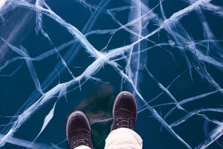 The feet of a female traveler on frozen transparent ice with cracks. Frozen Lake Baikal. Winter trip.の写真素材