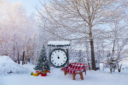 A Christmas tree with toys, a huge clock, a bench with a blanket in the city park in winter....