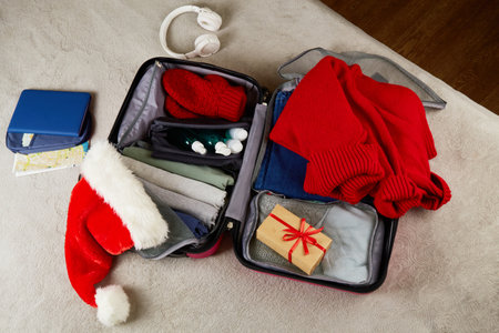 An open suitcase with clothes, documents, a gift, a Santa Claus hat. Packing things, preparing for a trip for the Christmas holidays. The concept of travel.の写真素材
