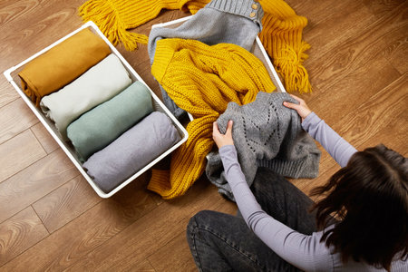 A young woman neatly puts stacks of knitted clothes into a metal laundry basket. The concept of...