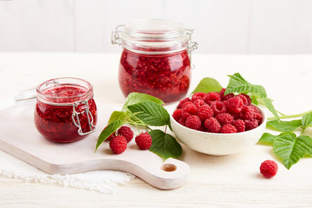 Homemade jam. Jars of raspberry jam and a bowl of fresh berries on a white wooden table.