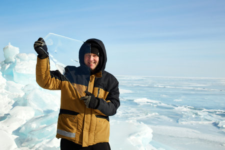A male traveler holds a transparent ice floe. Winter trip to the frozen Lake Baikalの写真素材