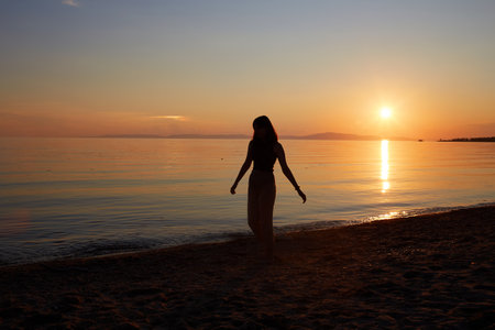 A pretty girl enjoys the sunset on a sandy beach. Summer travel, vacations at sea.の写真素材