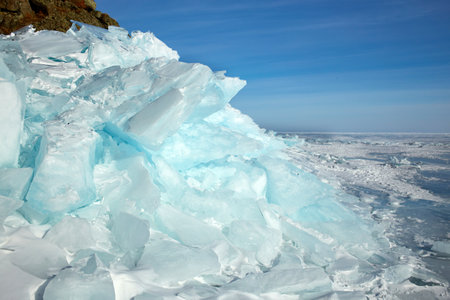 Huge blocks of transparent blue ice covered with snow, hummocks on the frozen Lake Baikal. Winter...