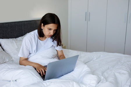 A young girl is working at a laptop in bed.の写真素材