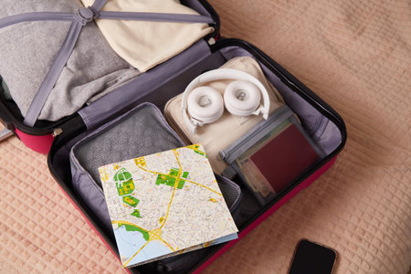 Open suitcase with clothes, a map, headphones, and documents for the trip. Travel conceptの写真素材