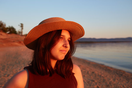 An attractive girl in a straw hat on a sandy beach at sunset. Summer travel, sea holidays.の写真素材