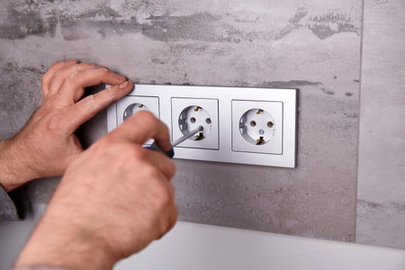 An electrician uses a screwdriver to install an electrical outlet on a wall covered with porcelain stoneware.の写真素材