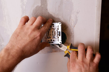 An electrician uses pliers to cut electrical wire while working on installing an electrical outlet