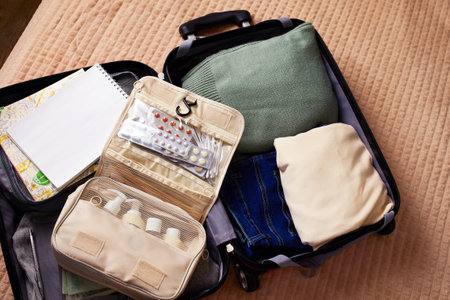An open suitcase with a travel set of cosmetics and hygiene products, clothes, a travel guide and other necessary things for the trip.の写真素材