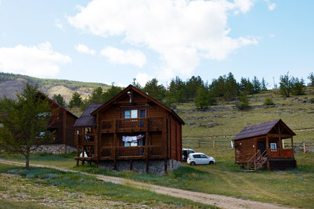 Rustic wooden cabins stand against a backdrop of hills and trees, creating a peaceful setting. A vehicle is parked nearby. The campsite is in a picturesque location.の写真素材