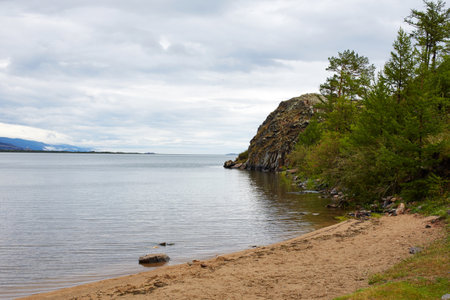 Rocky shore of a lake on a cloudy summer day. Pines and larches grow on the shore.の写真素材