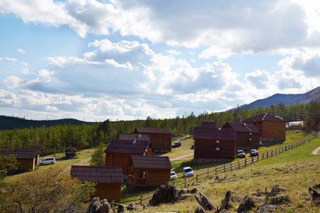 The campsite is located in a picturesque place. A tourist center with wooden houses in a rustic style against the backdrop of hills and trees. Tourists' cars are parked nearby.の写真素材