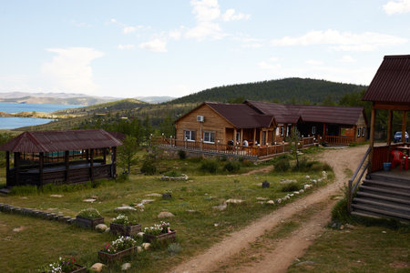 Wooden houses in a rustic style stand in a picturesque place against the backdrop of hills and trees, creating a peaceful atmosphere. Tourist base on the shore of Lake Baikalの写真素材