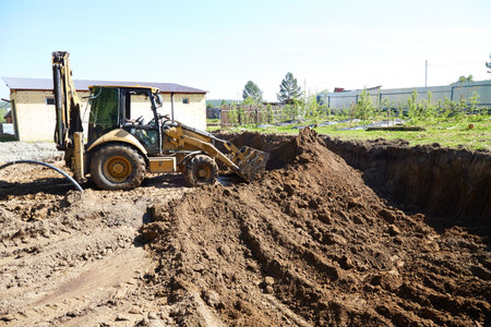 An excavator digs a deep excavation pit for building a house, loading soil. Building a house in rural areasの写真素材