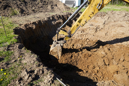 A digger operates in a rural setting, carefully excavating a deep trench.の写真素材